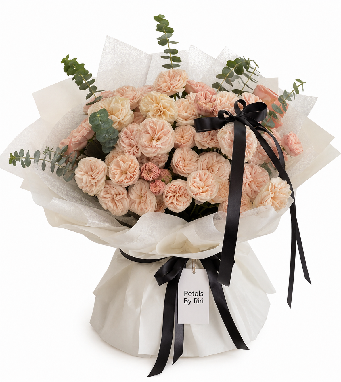 A bouquet of peach and pink carnations and roses wrapped in white tissue paper with a black ribbon and a tag that reads 'Petalis By Riri', set against a plain white background.